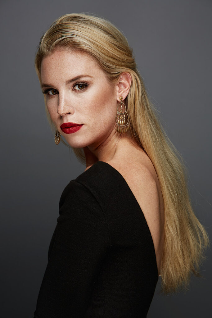 Editorial portrait of a blonde woman wearing a black dress and gold statement earrings, photographed by Rich Cirminello