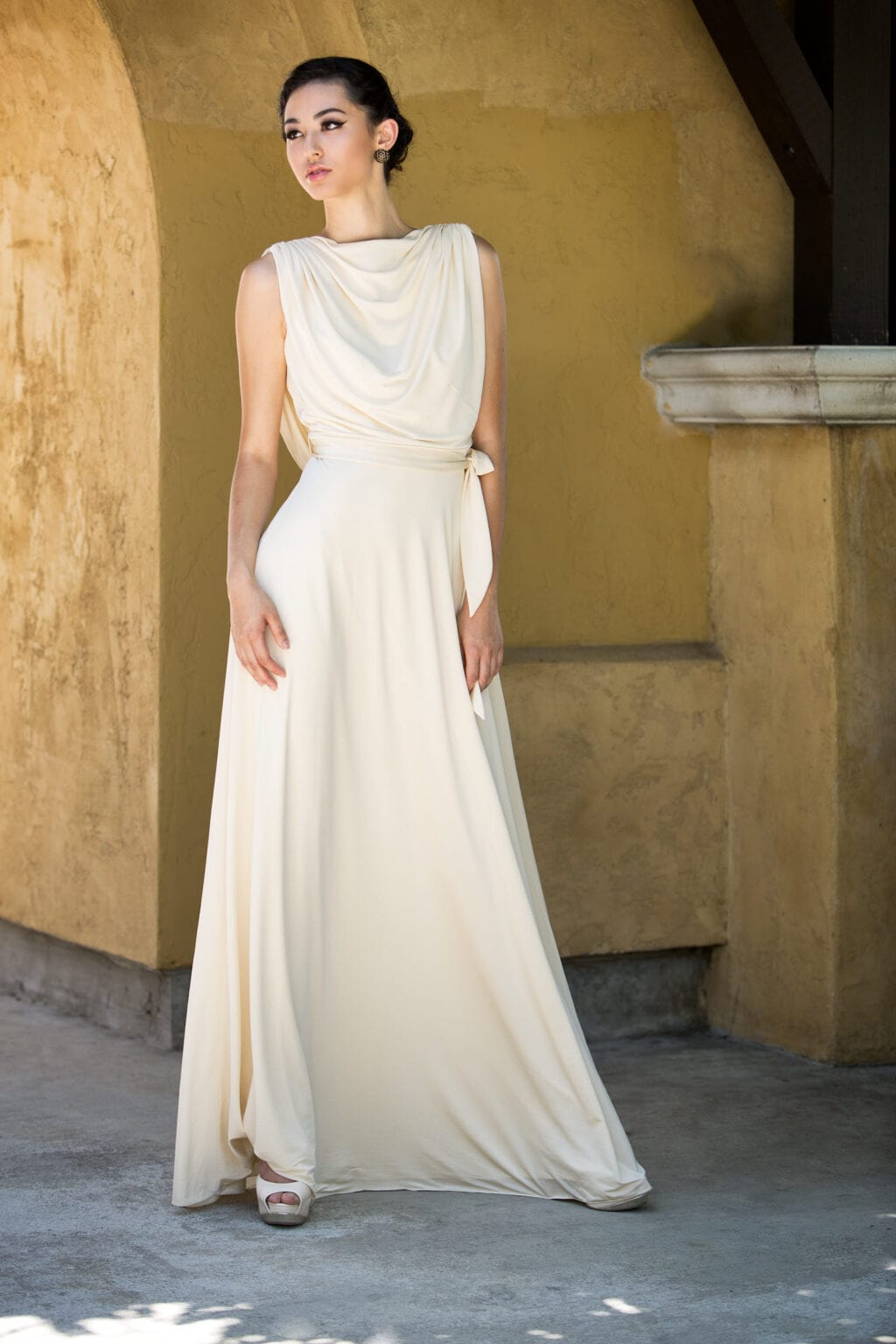 Model in a draped white gown standing beneath an arch.
