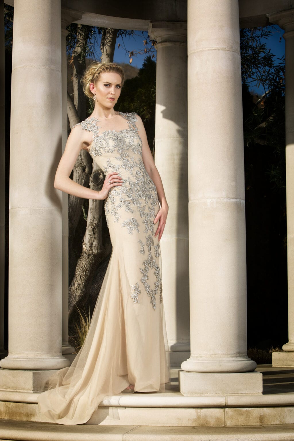 Model in a silver embellished ivory gown standing between columns.