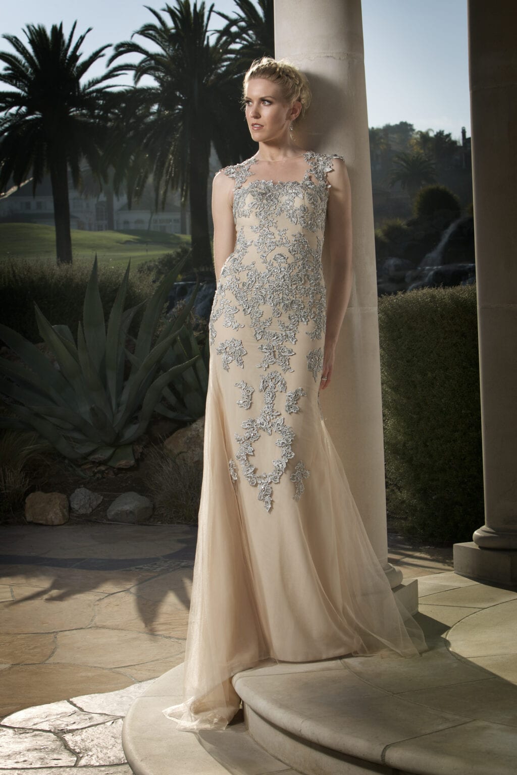 Model in an ivory embellished gown beside a column outdoors.