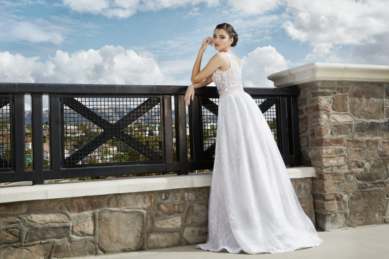 Model in a white bridal gown leaning on a terrace railing.