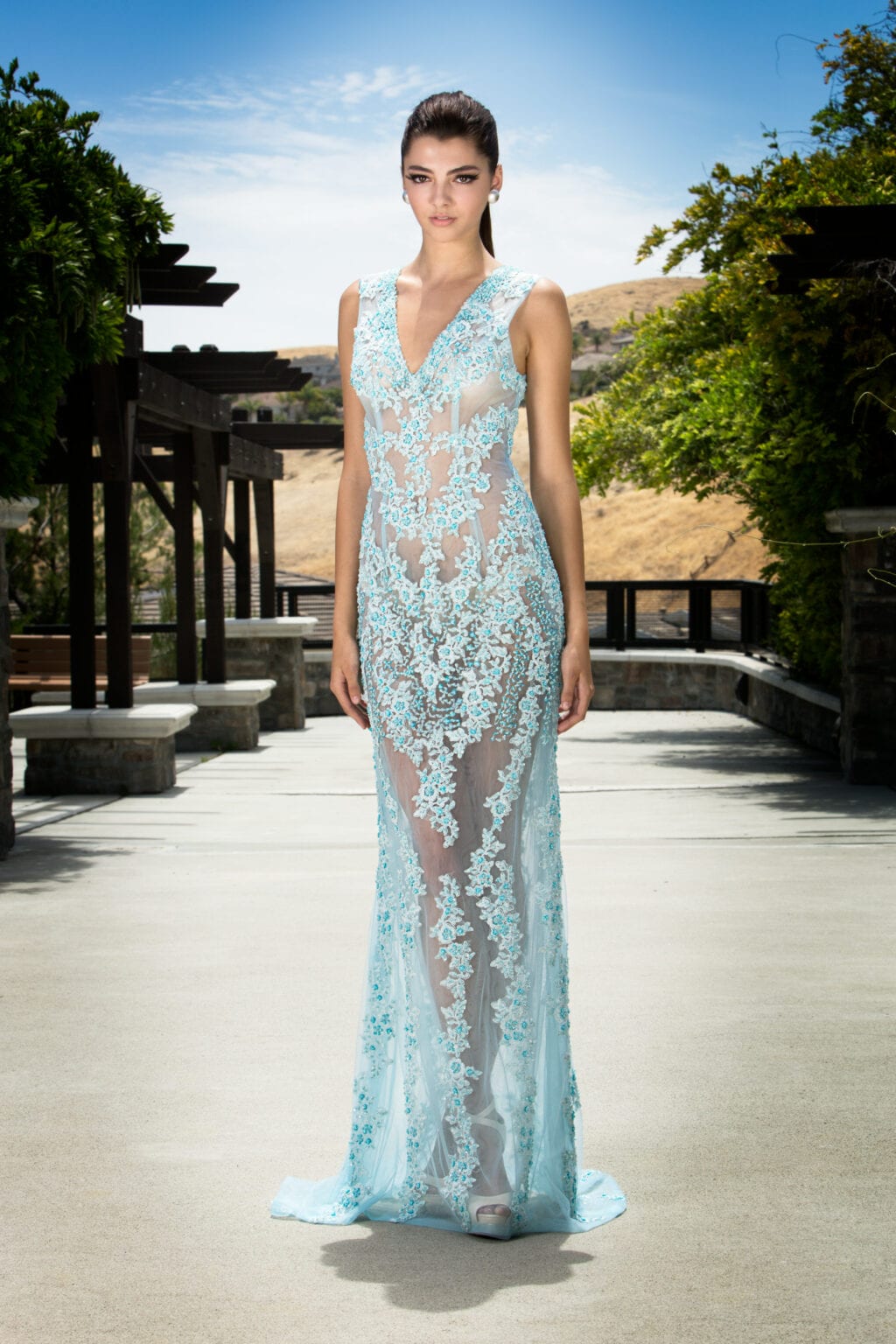 Model in a sheer light blue embellished gown outdoors.