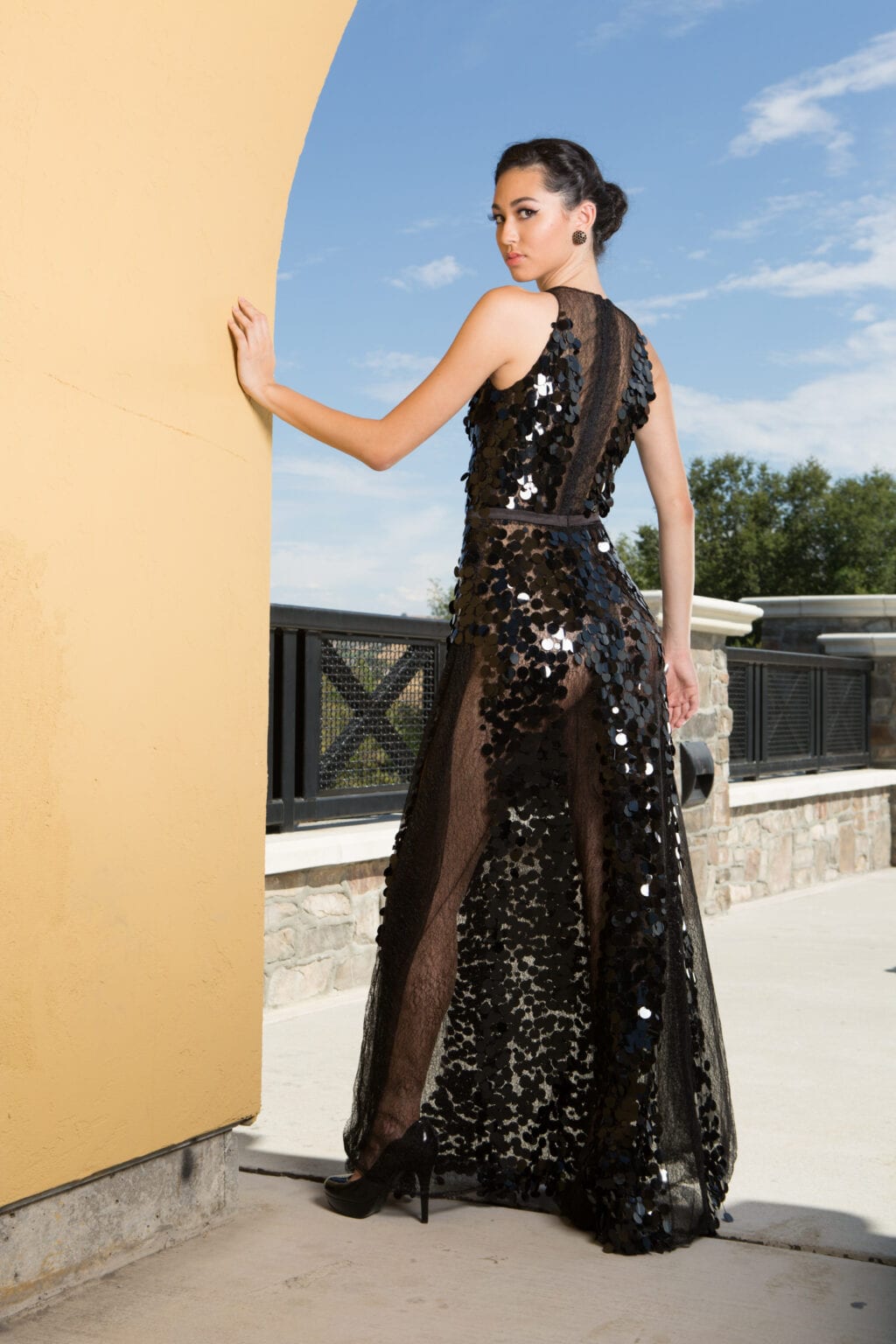 Back view of a model in a sheer black sequined gown on a terrace.