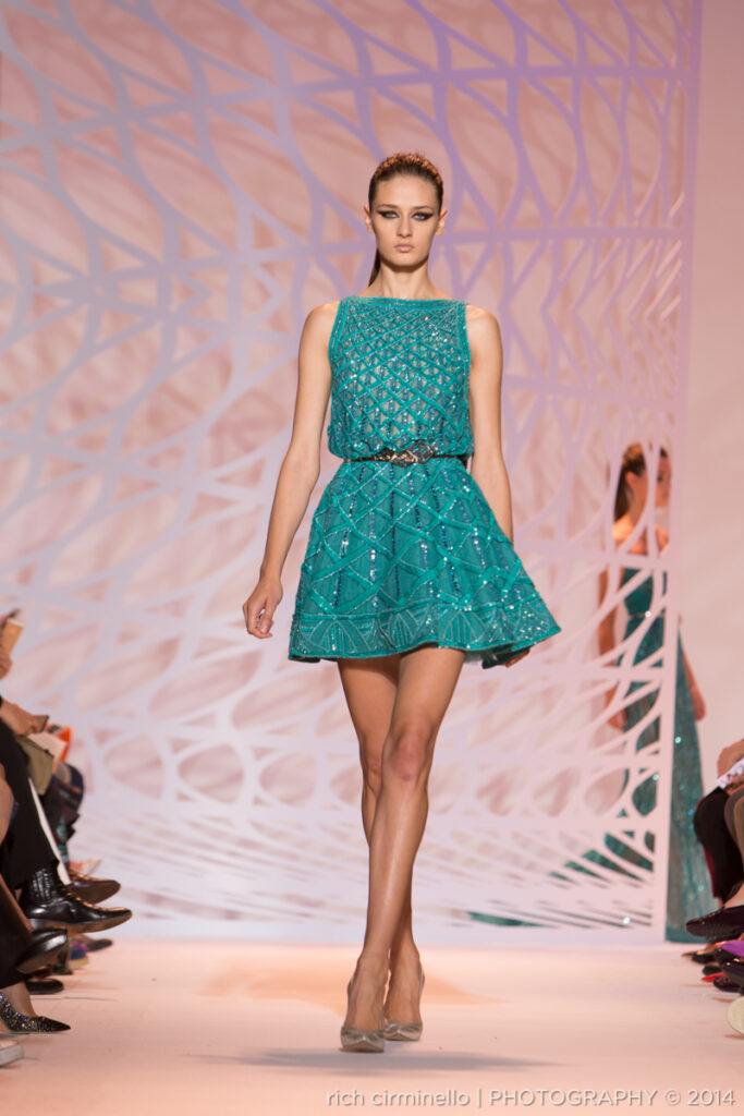 Model in a short teal Zuhair Murad dress walking the runway at Paris Haute Couture Fashion Week 2014. Photography by Rich Cirminello.